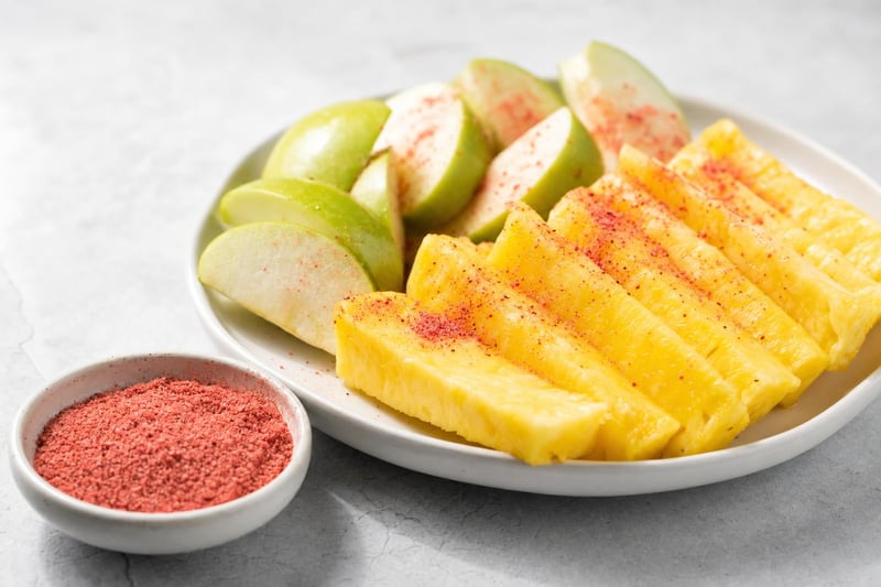 Dish of red li hing mui powder beside fresh pineapple and green apple slices dusted with it