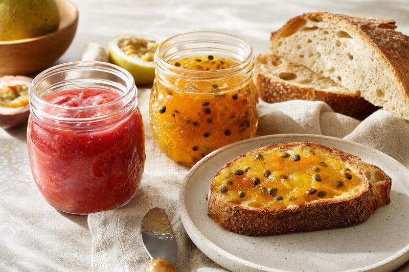 Jars of pink guava jam and golden lilikoi preserve beside toasted bread