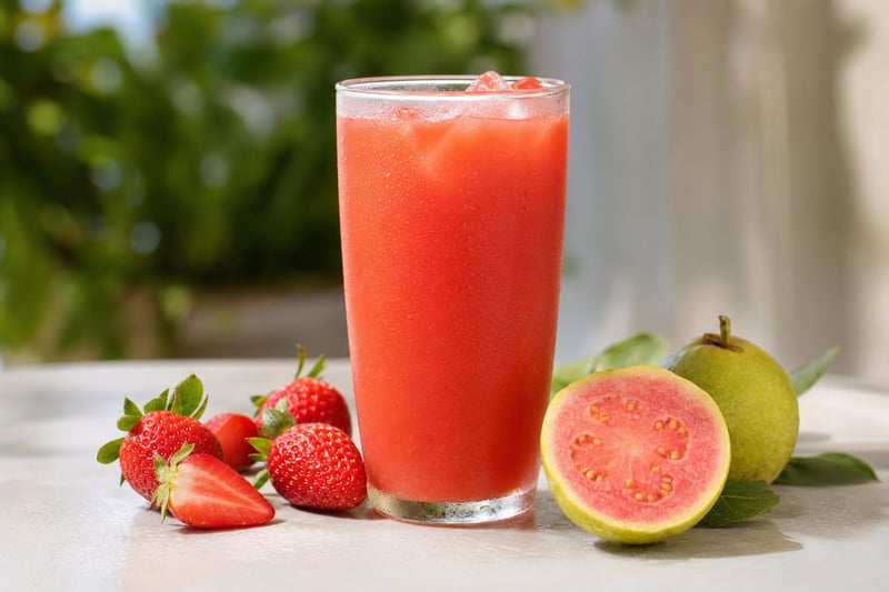 Tall glass of pink strawberry-guava juice with fresh strawberries and a halved guava